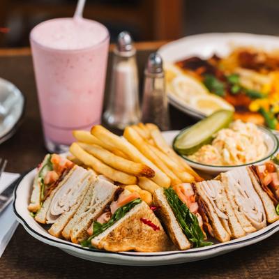 Turkey club sandwich served on a plate with fries and coleslaw.