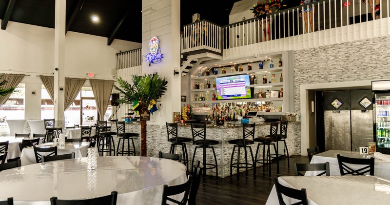 Interior of a modern restaurant featuring round tables, a bar with liquor bottles and a TV