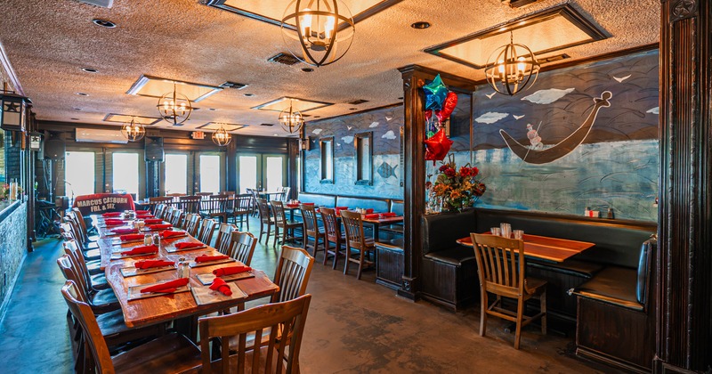 Warmly lit restaurant dining room with wood tables, red napkins, black booths