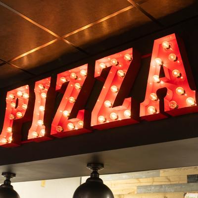Interior, a lighted sign reading Pizza on a wall above a counter.