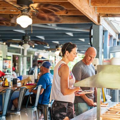 Exterior, two guests helping themselves to buffet food, a bar in the background.