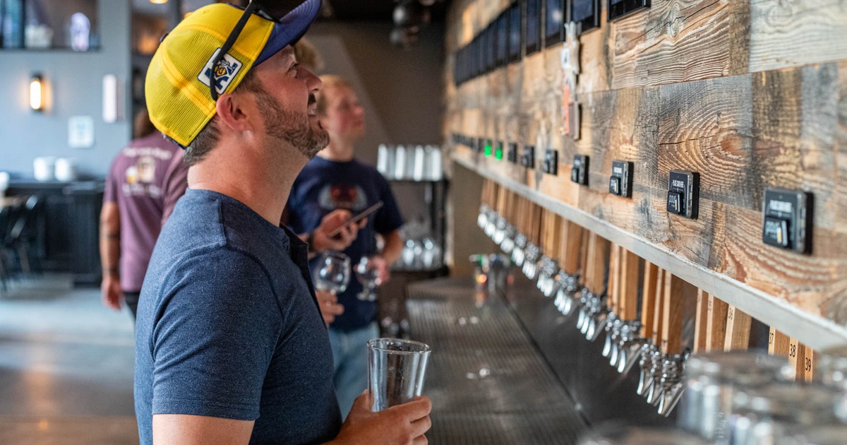 Customers hold glasses in front of a wall of beer taps