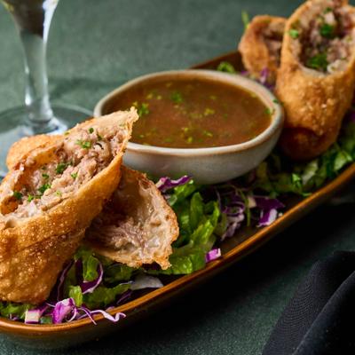 Philly Cheesesteak Egg Rolls served on a bed of lettuce, with a dipping sauce.