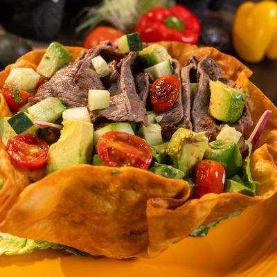 Beef taco salad with avocado, cucumbers, and tomatoes in a crispy tortilla bowl.