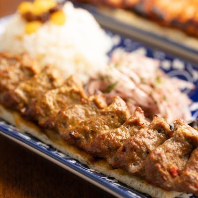 Adana Kebab served over pita bread with sides of rice and sliced onion.