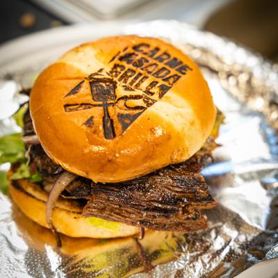 A Carne Asada Grill sandwich with the bun branded with a logo for the restaurant.