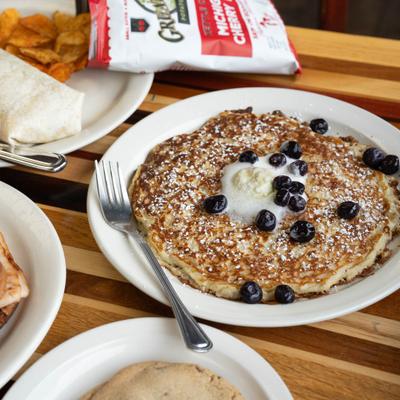 Pancakes topped with blueberries and melted butter, surrounded by a cookie and a bag of chips.