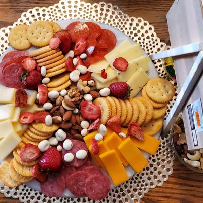 A round platter with assorted cheeses, meats, crackers, nuts, and strawberries.