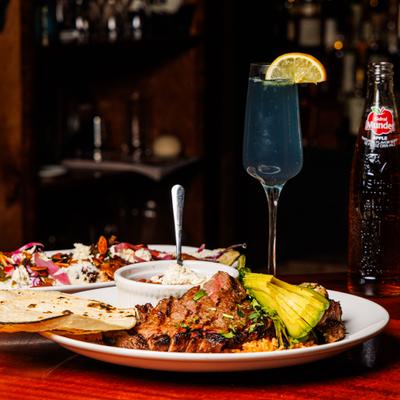 Steak and Drunken Beans  served alongside a cocktail and other dishes.