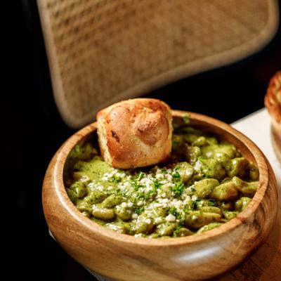 A wooden bowl filled with pesto gnocchi, topped with bread and cheese.