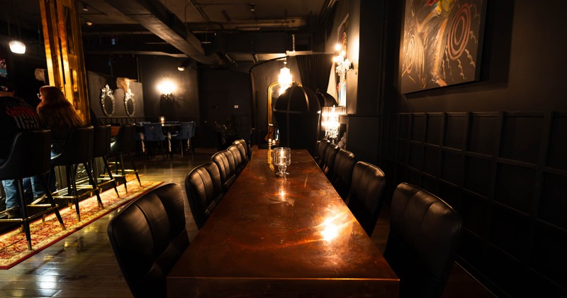 Inside, restaurant lounge, long dining table, dark chairs, warm lighting, and colorful wall art