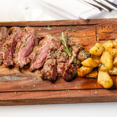 Slices steak garnished with herbs and served with roasted potatoes.
