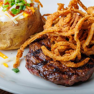 Steak with baked potato and onion strings.