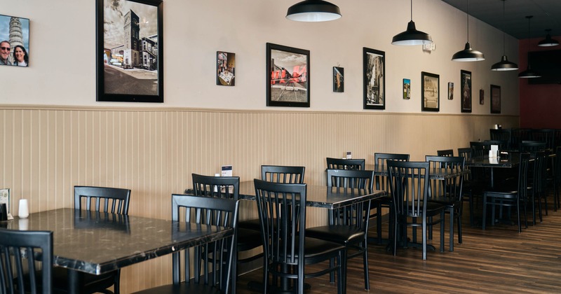 Interior of a restaurant with black tables and chairs, beige walls, framed photos, pendant lights