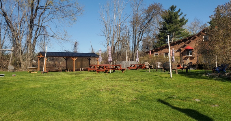 A backyard with wooden gazebo, picnic tables and seating, spacious lawn and trees