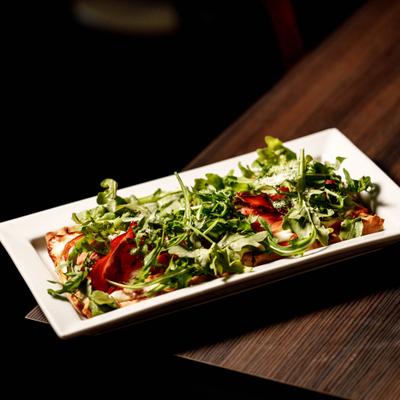 Margherita flatbread tooped with arugula, grated cheese and balsamic glaze.