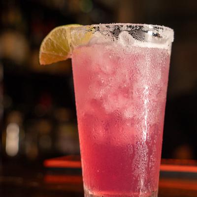 Pink margarita cocktail with a salt rim and lime wedge on a dark, reflective surface.