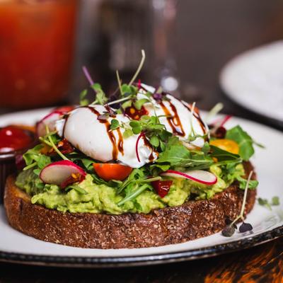 Avocado toast topped with poached eggs, arugula, sliced radishes, and microgreens.