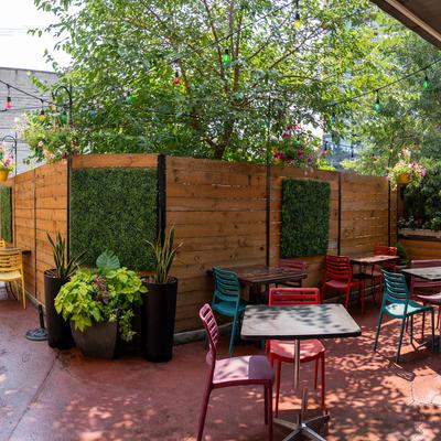 Outdoor patio with chairs and tables under string lights, lush greenery and wooden fences.