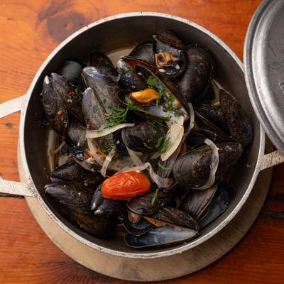 Pot of steamed mussels served with onions and cherry tomatoes.