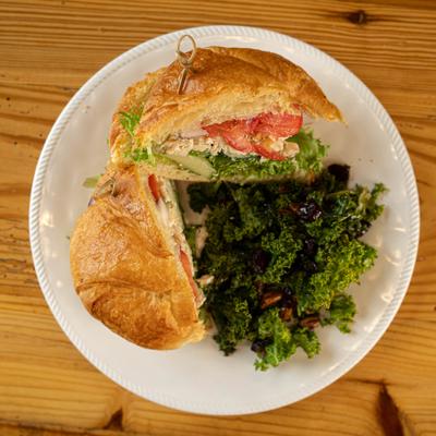 Top down view of Chicken salad croissant and a kale salad on a white plate.