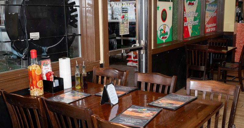 Interior with a wooden table, menus and condiments, next to windows showing event posters.