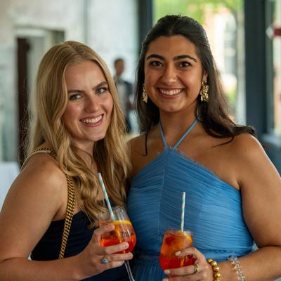 Two elegantly dressed friends enjoy drinks together at a celebration.