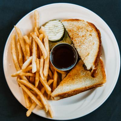 Brisket grilled cheese sandwich with fries, dipping sauce, and a slice of pickle.
