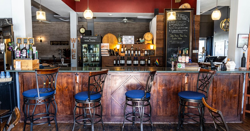 Interior of a wine bar with wooden counter, blue cushioned chairs, and hanging pendant lights