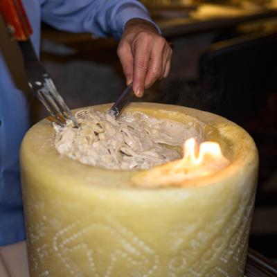 Pasta being tossed in a hollowed-out cheese wheel.