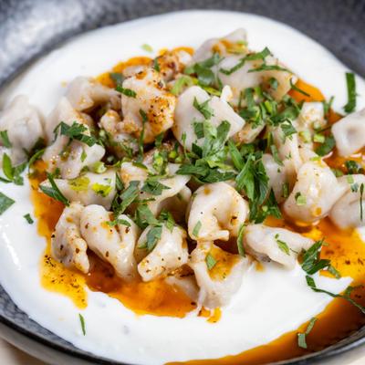 Small dumplings with herb garnish on yogurt sauce and spiced oil in a dark bowl.