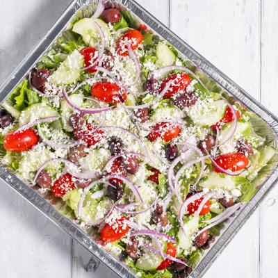 A large serving of Greek salad in a foil tray.