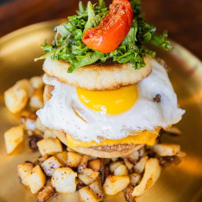 Breakfast sandwich featuring fried egg, melted cheese, fresh greens and a roasted tomato.