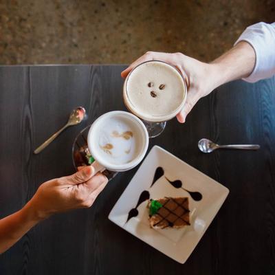 Two guests toasting with coffee and Espresso Martini at a table with served desserts, top view.