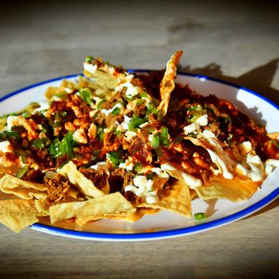 A plate of nachos topped with cheese, meat, scallions, and sour cream.