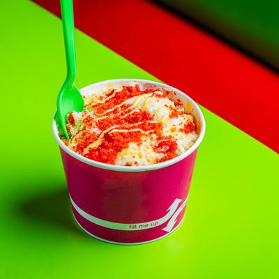 Mexican street corn served in a purple cup on a vibrant green table.