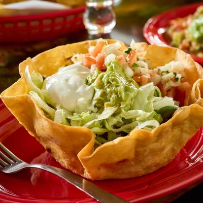 Taco salad in a crispy tortilla bowl topped with guacamole, sour cream, and salsa.