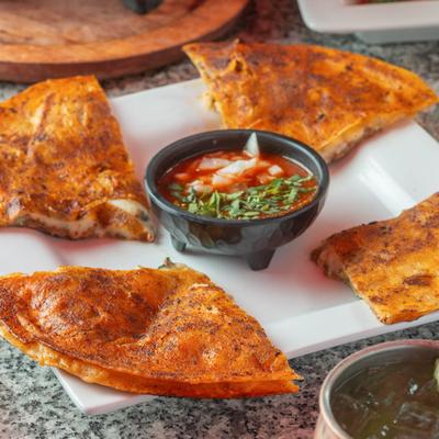 Quesabirria quesadilla served with a side of red consome topped with chopped onions and cilantro.