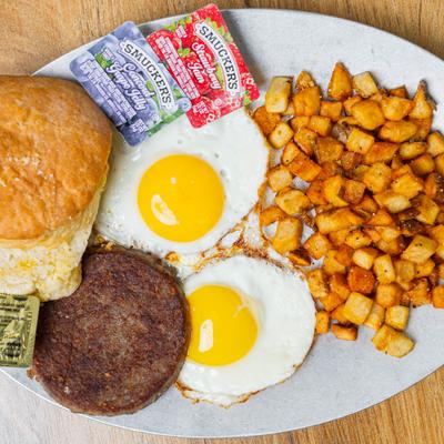Breakfast platter with fried eggs, sausage patty, home fries and a biscuit.