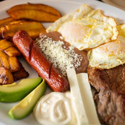 Steak and fried eggs, with refried beans, sausage, plantains, avocado, cheese.