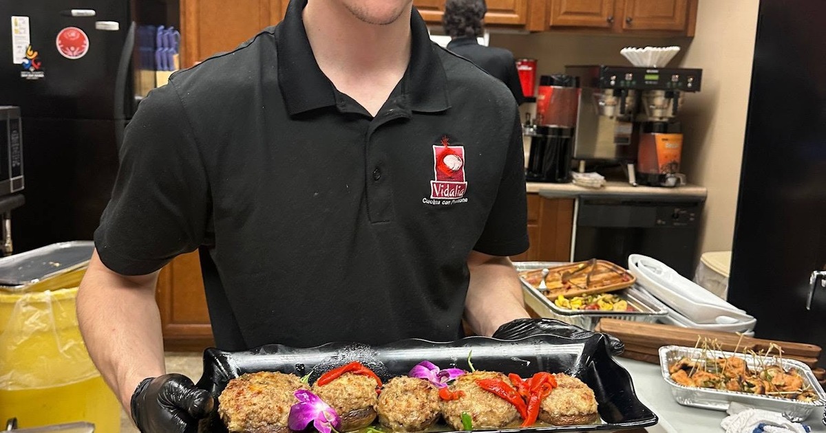 Staff member is wearing a polo shirt, holding a plate of food