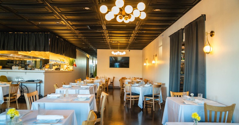 Interior, tables and chairs ready for guests, white cloths, bar in the back