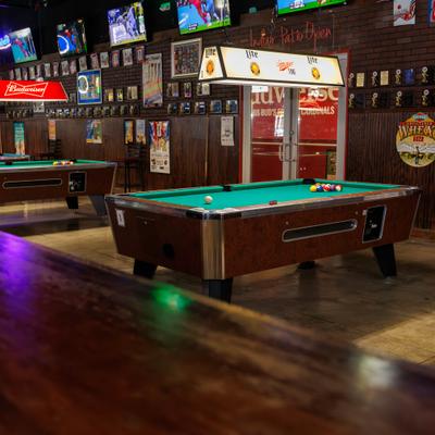 An indoor pool hall featuring several green-felt billiard tables under glowing light.