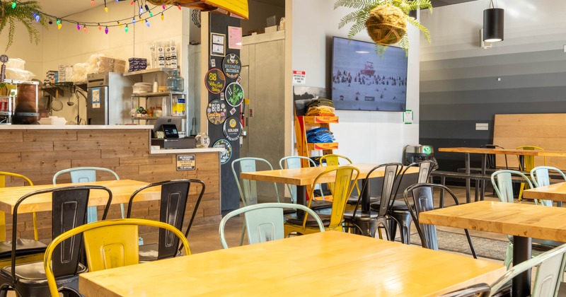 Interior, dining area, wooden top tables with metal chairs, kitchen entrance and checkout