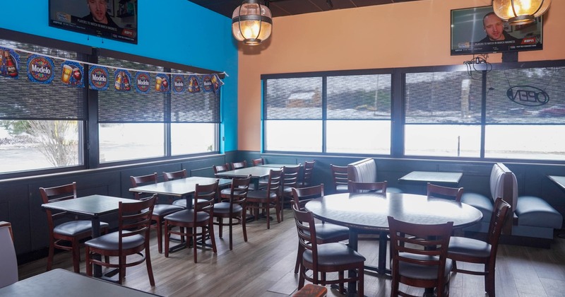 An empty restaurant dining area with wooden tables and chairs, large windows with shades