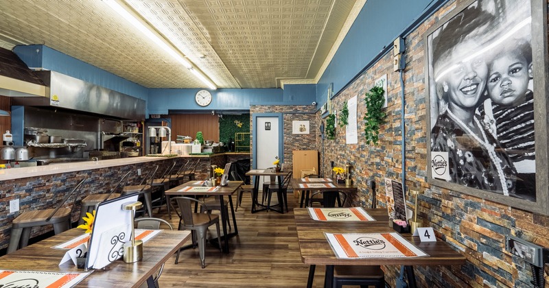 Interior of a cozy restaurant with wooden tables, brick walls, and a kitchen in the background