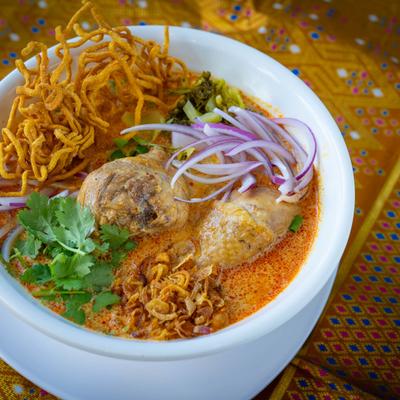 Noodles with chicken drumstick in yellow curry broth and veggie garnish.