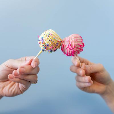Two hands holding lemon and strawberry cake pops.