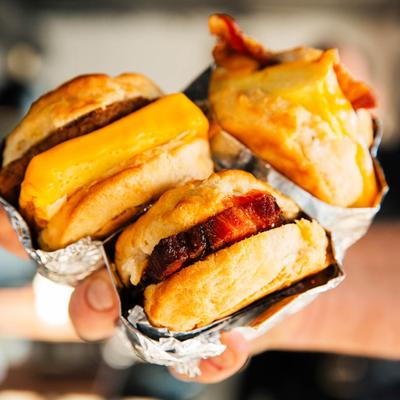 three breakfast sandwiches  (bacon, sausage, & egg) held together in a hand.