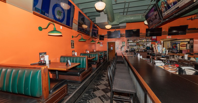 Interior of a lively bar with green booths and a long bar counter, TVs and orange walls.